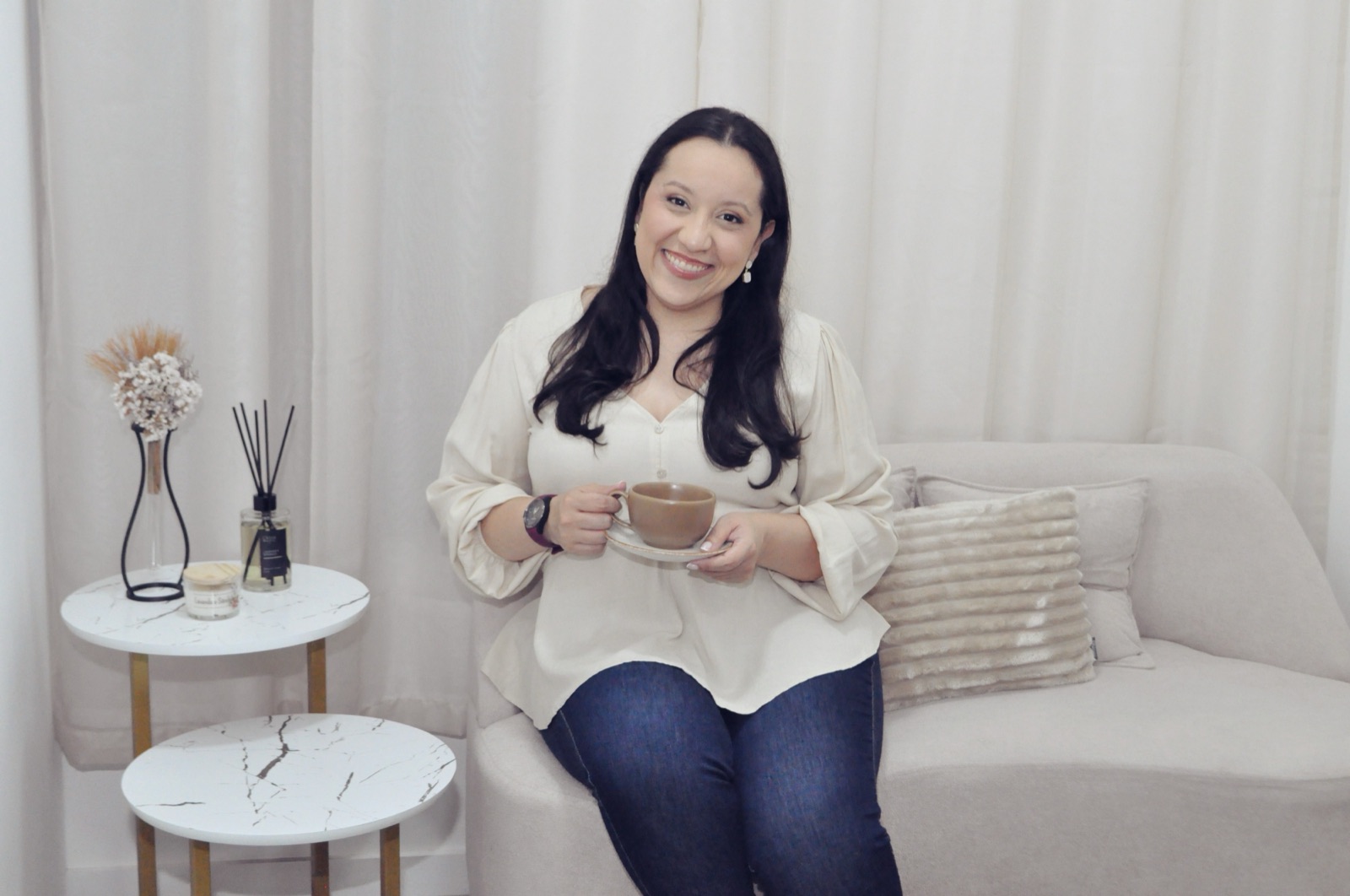 Lauren Perdigão sentada, sorrindo, segurando uma xícara de chá em seu consultório acolhedor
